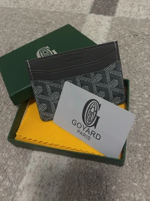 Goy4ard plånbok grå - Snyggt och stilrent kortfodral från Goy4ard i grått med klassiskt mönster och logotyp. Fodralet är tillverkat i läder och har flera fack för kort. Kommer med original ask och tygpåse. Perfekt för dig som vill ha något exklusivt och trendigt.