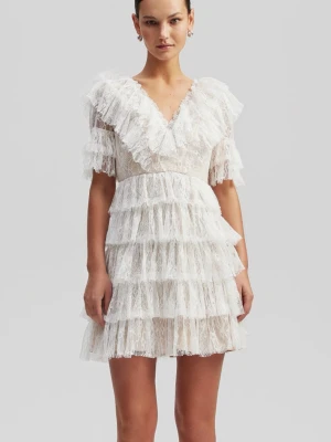 Vit spetsklänning med volanger - Säljer en kort vit klänning med flera lager volanger och v-ringad hals. Klänningen är gjord i spets och har korta ärmar med volangdetaljer. Perfekt för dig som tar studenten i sommar.