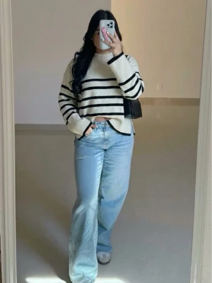 Randig stickad tröja i vitt och svart - Säljer en snygg stickad tröja i vitt med svarta horisontella ränder. Tröjan har en avslappnad passform, rund halsringning och långa ärmar. Perfekt för dig som gillar en enkel men trendig look.