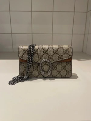 Axelväska  - En stilren och snygg axelväska i beige färg. Kan även bäras som en crossover bag då kedjorna går att förlänga. Helt ny, topp kvalite 🤍