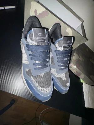 Valentino Garavani ruckrunners - Snygga sneakers från Valentino Garavani i blått, grått och vitt med coolt kamouflagemönster. Skorna har snörning, meshdetaljer och mockapartier för en modern och sportig look. Perfekta för dig som vill sticka ut med stilrena och exklusiva sneakers.