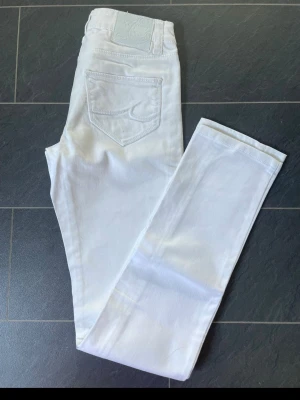 Vita jeans från Crocker 26/32 - Snygga vita jeans från Crocker med klassisk femficksmodell och broderad detalj på bakfickan. Jeansen har raka ben och är tillverkade i ett mjukt denimtyg som ger en clean och fräsch look. Perfekta för dig som vill sticka ut med stilrena vita jeans.