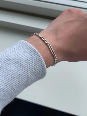 Silver kedjearmband - Stilrent armband i silver med klassisk kedjedesign. Armbandet har en enkel karbinhake som lås och passar perfekt för dig som gillar minimalistiska accessoarer. Materialet är silver och länkarna är platta och blanka.