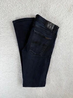 Nudie jeans Tube Tom W32 L34 - Snygga mörkblå skinny jeans från Nudie Jeans med klassisk femficksdesign och subtila slitningar. Jeansen har en smal passform och är tillverkade i stretchigt denim för extra komfort. Perfekta för en trendig och avslappnad stil.