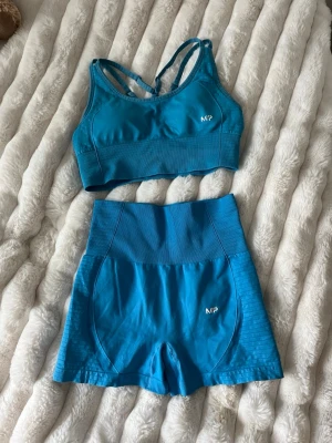 Blått träningsset från MP - Snyggt blått träningsset från MP med sport-bh och matchande shorts. Sport-bhn har smala korsade axelband och shorts med bred midjeresår för extra stöd. Perfekt för gymmet eller löpning. Materialet är stretchigt och följsamt för maximal komfort. Säljer för jag har så mycket träningskläder