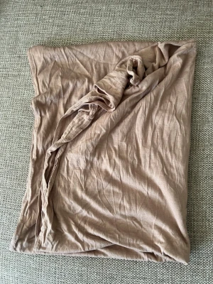 Beige sjal i mjukt tyg jearsy - En stor, rektangulär beige sjal i tunt och mjukt material. Perfekt att svepa runt halsen eller använda som accessoar. Enkel och stilren design som passar till många outfits.