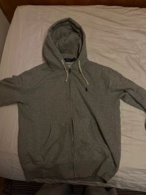 Grå zip-up från Ralph Lauren - Hej! Jag säljer min mans Ralph Lauren Zip-Up då han tyvärr inte har användning för den längre då den är för liten för honom nu! Den har varit använd ett par gånger men är fortfarande i ett väldigt bra skick! Kvitto finns för äkthetsbevis!