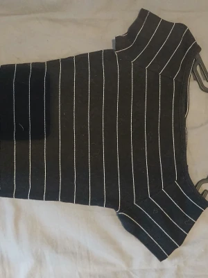 Svart ribbad randig topp Kappahl - Svart ribbad topp från Kappahl med vita lodräta ränder. Kortärmad modell med rund halsringning och stretchigt material som sitter snyggt på kroppen. Perfekt till jeans eller kjol för en stilren look.