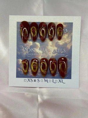 Ember (S);Medium Almond - Handgjorda press-on naglar i vinröd färg med cirklar i cateye i guld. Naglarna har en elegant medium lång almondform och är tillverkade i S: 15 mm, 11,5 mm, 12 mm, 11 mm, 9 mm . Perfekt för dig som vill ha en trendig och personlig look.
