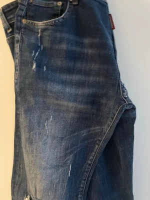 Mörkblå slitna jeans med raka ben - Säljer ett par mörkblå jeans med slitningar och raka ben. Jeansen har klassisk femficksdesign och synliga slitdetaljer framtill för en cool, avslappnad look. Perfekta för dig som gillar en trendig streetstil.