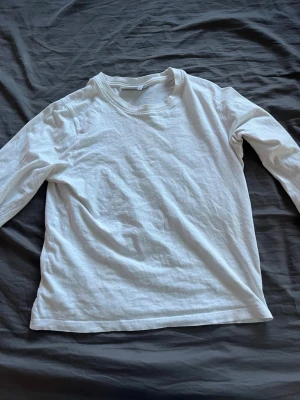 Vit långärmad topp i bomull - En basic vit långärmad topp i mjuk bomull. Enkel och stilren design med rund halsringning, perfekt att matcha med olika outfits. Skön passform och passar till många tillfällen.