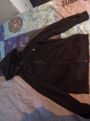 Svart Polo Ralph Lauren zip-hoodie - Svart hoodie med dragkedja från Polo Ralph Lauren. Klassisk modell med huva och fickor framtill. Liten broderad logga på bröstet. Perfekt för en chill och stilren look. Mjuk bomullskänsla och snygg passform.