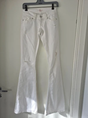 Vita utsvängda jeans - Snygga vita jeans med utsvängda ben. Modellen är low rise och har slitna detaljer på låren och knäna. Klassisk femficksdesign och bälteshällor.