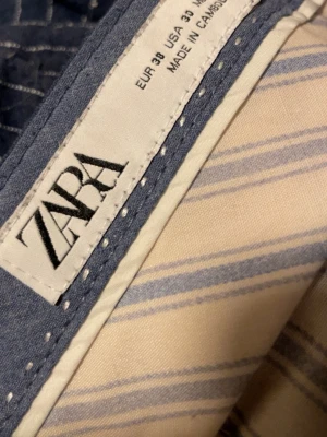 Blå randiga byxor från Zara - Snygga blå byxor från Zara med vita tunna ränder. Byxorna har knapp och dragkedja framtill och är perfekta för en trendig look. Tillverkade i ett mjukt material som känns bekvämt hela dagen.