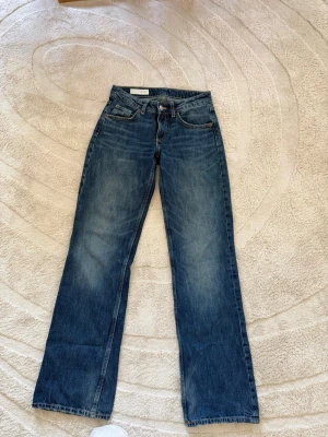 Blå raka jeans från Acne Studios - Säljer ett par klassiska blå jeans från Acne Studios med rak passform och fem fickor. Jeansen har snygga slitningar och kontrastsömmar, tillverkade i kraftig denim. Perfekta för en avslappnad och trendig look.
