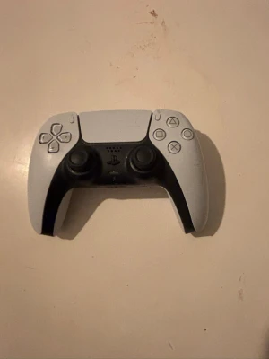 Vit PlayStation 5 DualSense handkontroll - Säljer en vit och svart PlayStation 5 DualSense handkontroll från Sony. Kontrollen har en modern design med tydliga knappar, två analoga spakar och touchpad. Tillverkad i plast och passar perfekt för gaming på PS5.
