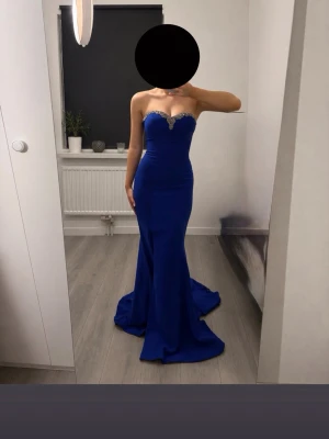 Blå långklänning med pärldetaljer stl xs-s - Elegant blå långklänning med figurnära passform och axelbandslös design. Klänningen har vacker pärldetalj vid bysten och en lätt utsvängd nederdel med en diskret slits. 