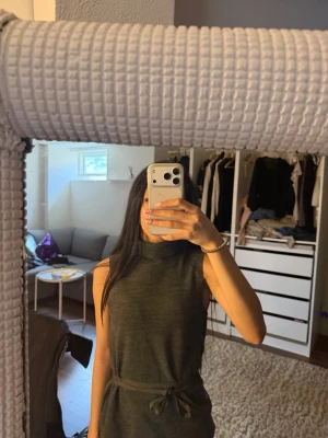 Mörkgrå ärmlös polotopp med knyt - Säljer en mörkgrå ärmlös polotopp med hög krage och knytband i midjan. Toppen har en clean och stilren look, perfekt att matcha med jeans eller kjol. Materialet känns mjukt och stretchigt, vilket gör den bekväm att bära hela dagen.