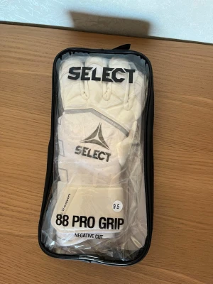 Select Målvaktshandskar 88 Pro Grip V25 - Vit/Grå 9.5 - Storlek 9.5. Nyskick.          88 Pro Grip från Select är en avancerad målvaktshandske utvecklad för både träning och match på högsta nivå. Den används av professionella målvakter och är konstruerad med lättviktsmaterial och högkvalitativt 3 mm Pro Tech Latex för att ge ett optimalt grepp i alla situationer. Handsken har perforerat airprene för förbättrad ventilation, vilket bidrar till ökad komfort under spelet. På ovansidan av fingrarna finns en strategiskt placerad "punch zone" som ger extra 