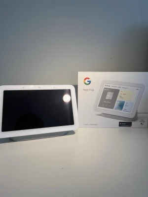 Google Nest Hub 2nd Gen smartskärm - Google Nest Hub 2nd generation med vit ram och grå tygbas. Smartskärm med touchdisplay, röststyrning via Google Assistant och inbyggd högtalare. Perfekt för att styra smarta hemmet, visa bilder, kolla väder och spela musik. Strömadapter medföljer.