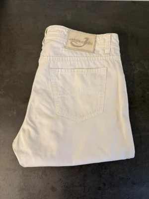 Vita jeans från Jacob Cohen stl 34 - Snygga vita jeans från Jacob Cohen med klassisk femficksmodell och raka ben. Jeansen har en ljus etikett bak i midjan och silverfärgade nitar. Perfekta för en fräsch och stilren look. Hör av dig om du vill ha alla mått!