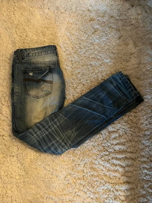 Blå slitna nudie selvedge jeans med detaljer - Säljer ett par blå nudie selvedge med slitningar och tvättade effekter. Jeansen har raka ben, klassiska bakfickor med slitna detaljer och kontrastsömmar. Materialet är denim och de har en cool, avslappnad look. Storleken är 29/32