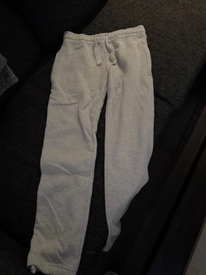 Russemerch byxor  - Säljer ett par ljusgrå russemerch byxor med resår och dragsko i midjan. Byxorna har två sidofickor fram och en bakficka. De är raka i modellen och har mjukt, bekvämt material som passar perfekt för chill dagar hemma eller när du vill vara extra bekväm.