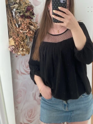 Svart blus med meshdetalj - Svart blus med transparent mesh upptill och små prickar. Vida, trekvarts ärmar med knapp vid ärmslut och lös passform. Rund halsringning.Två laggade hål upptill på ryggen(syns ej om håret är utsläppt)❣️