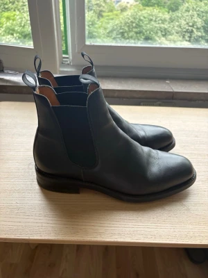 Svarta Chelsea boots från Sebago - Stilrena svarta Chelsea boots från Sebago i äkta läder med klassisk resår på sidorna och dragflikar fram och bak. Skorna har en låg klack och rundad tå, samt ljusbrunt läder på insidan. Perfekta för en snygg och tidlös look.