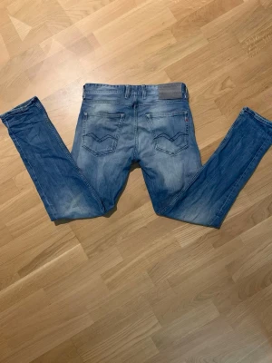 Blå slim fit jeans från Replay - Snygga blå slim fit jeans från Replay med klassiska fem fickor och diskreta slitningar. Jeansen har raka ben och tydliga sömmar på bakfickorna. Storlek: 27/30