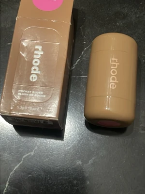 Rhode Pocket Blush 'Sprinkle' - Rhode Pocket Blush i färgen 'Sprinkle' är ett krämrouge i stickformat. Förpackningen är beige och kompakt, perfekt att ta med i väskan. Färgen 'Sprinkle' är en livlig rosa nyans som ger kinderna en fräsch och ungdomlig look.