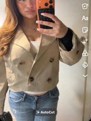 Beige croppad kavaj med knappar - Trendig croppad kavaj i beige med dubbelknäppning och stora bruna knappar. Kavajen har bred krage och en loose passform, perfekt att styla med jeans eller kjol. Snygg och enkel att matcha till olika outfits.