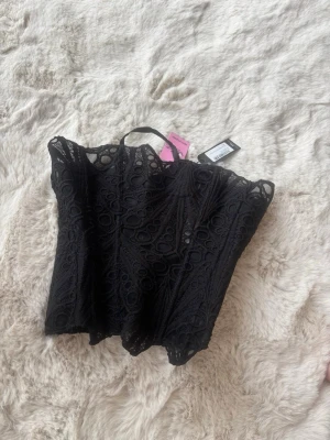 Svart spetskorsett från prettylittleting - Trendig svart korsett  i spets med snyggt mönster och transparenta detaljer. Perfekt att styla med jeans eller kjol för en cool look. Axelbandslös design och figurnära passform.