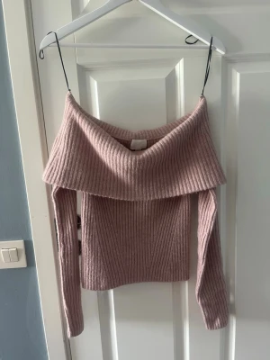 Ljusrosa off shoulder stickad tröja - Trendig ljusrosa stickad tröja med bred off shoulder-krage och ribbstickat mönster. Långa ärmar och mjukt material som ger en avslappnad men snygg look. Perfekt för dig som vill ha en mysig men stilren vibe. Helt ny💕