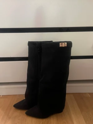 ❤️Svarta knähöga boots med gulddetalj❤️ - Snygga svarta knähöga stövlar i mockaimitation med spetsig tå och guldfärgad spänndetalj upptill. Dragkedja på insidan för enkel påtagning. Perfekta för att lyfta din outfit med en trendig touch.