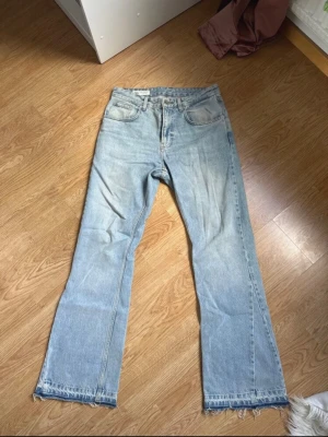 Ljusblå raka jeans från zara med rå kant - Säljer ett par ljusblå jeans med rak passform och rå, fransad kant nertill. Jeansen har klassisk femficksdesign och hög midja. Perfekta för en avslappnad och trendig look. Materialet är denim i 100% bomull.