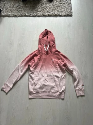 Rosa ombre hoodie från Hollister - Snygg hoodie från Hollister i en rosa ombre-färg som går från mörkare rosa upptill till ljusare nedtill. Klassisk huva med vita snören och magficka framtill. Liten Hollister-logga broderad på bröstet. Perfekt för en avslappnad och trendig stil.
