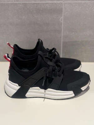 Svarta Moncler sneakers med vit sula - Stilrena Moncler Luvarove sneakers i storlek 41. Skorna kommer med orginallåda samt dustbag. De är använda 3-4 gånger och har små tecken på användning, se bilder. Hör av er vid intresse eller vid önskan om fler bilder. Äkthetsbevis medföljer!