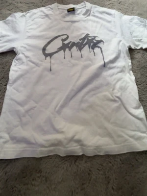 Vit t-shirt med graffiti-tryck - Säljer en vit t-shirt med ett stort grått graffiti-inspirerat tryck på bröstet. T-shirten har rund hals och korta ärmar. Perfekt för dig som gillar streetwear och vill sticka ut med en unik design.