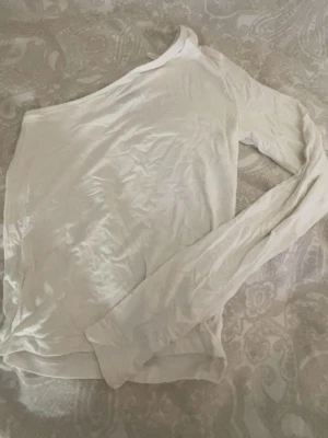 Vit oneshoulder topp från Gina Tricot - Snygg vit oneshoulder topp från Gina Tricot med lång ärm på ena sidan. Tunn och mjuk känsla, perfekt att styla med jeans eller kjol. Enkel och stilren design som passar till många olika looks.