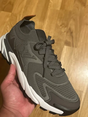 Grå lv sneaker - Snygg grå sneaker från Lv med chunky vit sula och detaljer i mesh och syntet. Skon har en modern design med svarta och grå inslag, samt snörning framtill. Perfekt för dig som gillar streetwear och stilrena sneakers.
