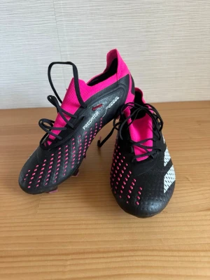 Adidas Predator svart/rosa fotbollsskor - Säljer ett par Adidas Predator fotbollsskor i svart och rosa. Snygg design med bra kontroll och skön passform. Passar både träning och matchspel.  * Predator-modell * Bra skick * Lätta och bekväma * Passar gräs/konstgräs * Storlek: 41 1/3