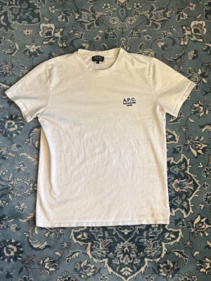 A.P.C T-Shirt Vit - Riktigt clean T-shirt från APC i gott skick och najs fit. Mått: bröstvidd: 50cm. Total längd: 68cm