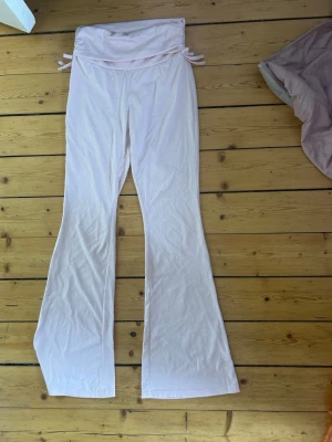 Ljusrosa loungebyxor med utsvängda ben - Mysiga ljusrosa loungebyxor med bred linning och knytband i sidorna. Byxorna har utsvängda ben och är tillverkade i ett mjukt, stretchigt material som känns skönt mot huden. Perfekta för chill dagar hemma eller när du vill ha det extra bekvämt.