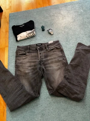 Grå slim fit jeans från Jack & Jones - Snygga grå slim fit jeans från Jack & Jones med klassisk femficksdesign och dragkedjegylf. Jeansen har en tvättad look och smal passform som sitter tajt längs benen. Perfekta för en trendig och avslappnad stil. 