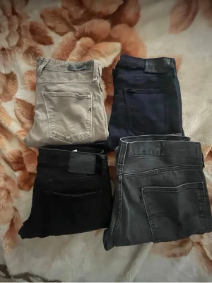 Fyra par jeans i olika färger - Säljer fyra par jeans i olika färger: ett par ljusbeige, ett par mörkblå, ett par svarta och ett par grå. Klassisk femficksmodell med raka ben. Perfekta för dig som vill variera din stil med olika basfärger. Materialet är denim.Replay 33w Jack Jones 30w Lee 29w Levis 36w