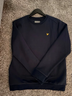 Mörkblå sweatshirt från Lyle & Scott - Snygg mörkblå sweatshirt från Lyle & Scott med klassisk rund hals med  logotyp på bröstet. Tröjan har långa ärmar och ribbade muddar vid ärmslut och nederkant. Inga defekter 