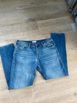Blå tapered jeans från Jack & Jones - Snygga blå jeans från Jack & Jones i modellen Tapered/Mike. Jeansen har klassisk femficksdesign, normalhög midja och avsmalnande ben. Tillverkade i denim med lätt tvättad look och slitningar för en avslappnad stil.
