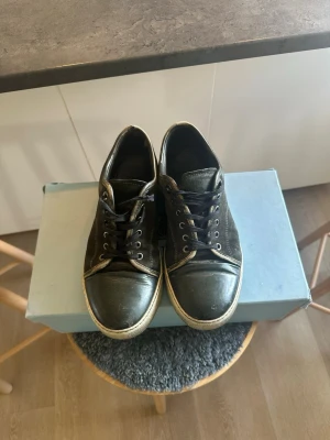 Svarta låga sneakers med vita sulor - Svarta sneakers med lågt skaft och vita sulor. Skorna har svarta snören, tåhätta i läder och ovandel i mocka eller canvas. Klassisk design som passar till det mesta och ger en avslappnad vibe.