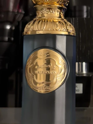 Gissah imperial valley parfym - Lyxig parfymflaska från Widian Gold Collection med elegant svart och guld design. Flaskan har en matt svart kropp och detaljer i blankt guld, inklusive ett dekorativt emblem och lock. Perfekt för dig som gillar exklusiva dofter och snygg inredning på parfymhyllan.